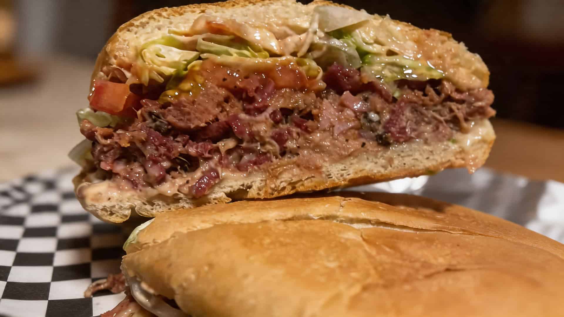Close-up of a Puerto Rican sandwich cut in half showing layered meat and fresh toppings
